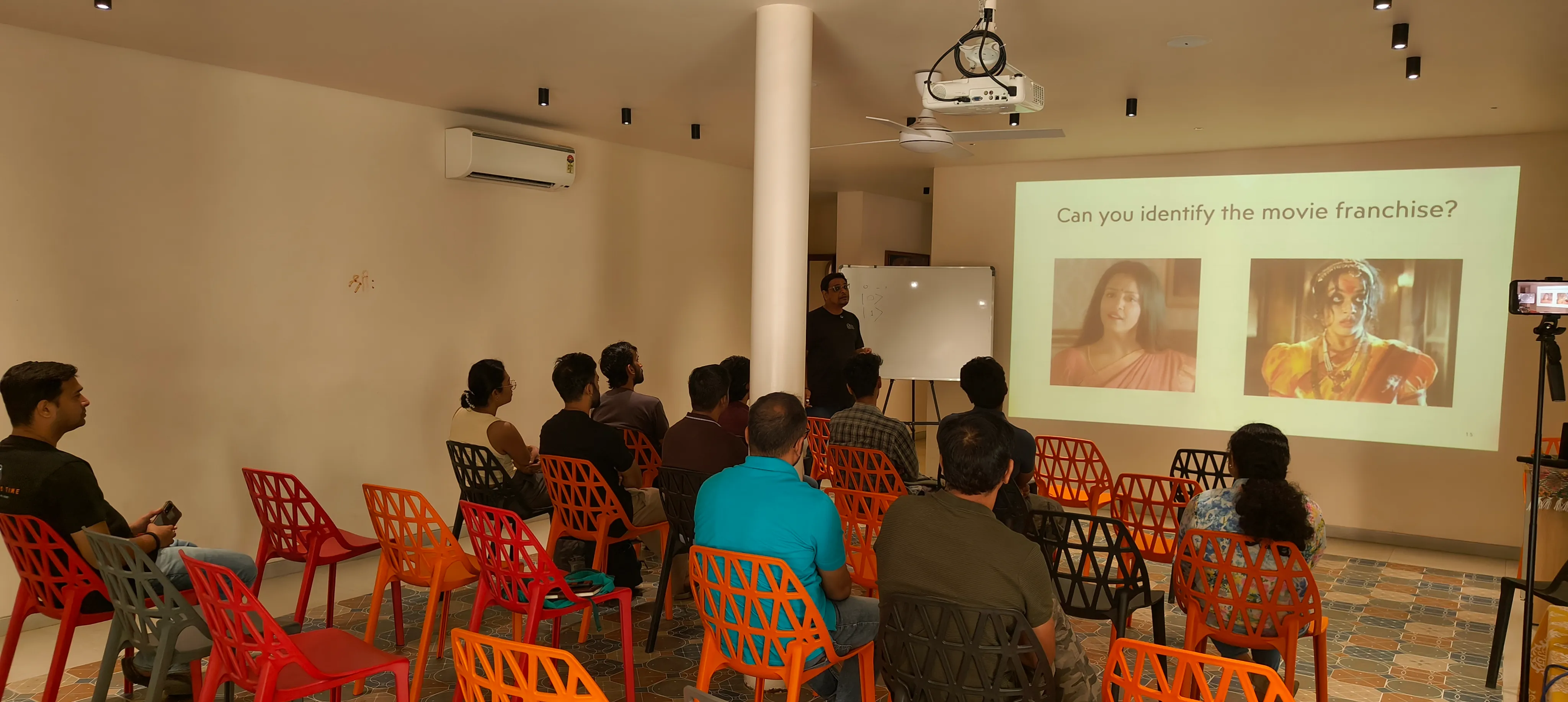 A speaker at the front of a bright room opening with a film analogy slide, Ganga and Chandramukhi, for qubits, to a seated audience at the Quantum Circle